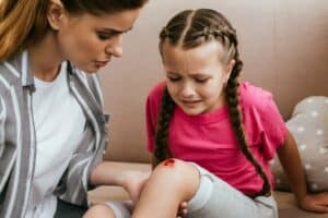 mother-holding-leg-with-wound-on-knee-while-daughter